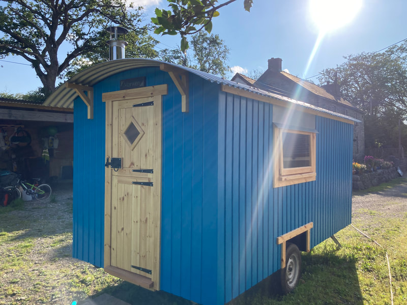 A bright blue shepherd's hut with a pale timber door, standing in a sunny garden.