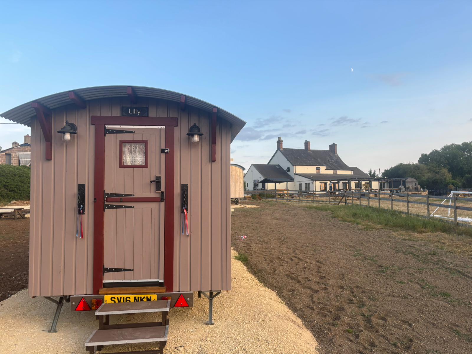 A dusky pink shepherd's hut named Lilly, with its steps down at a countryside pub.