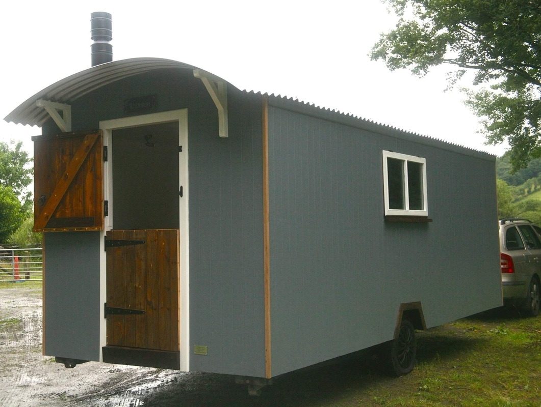 A slate grey shepherd hut with a timber stable door.