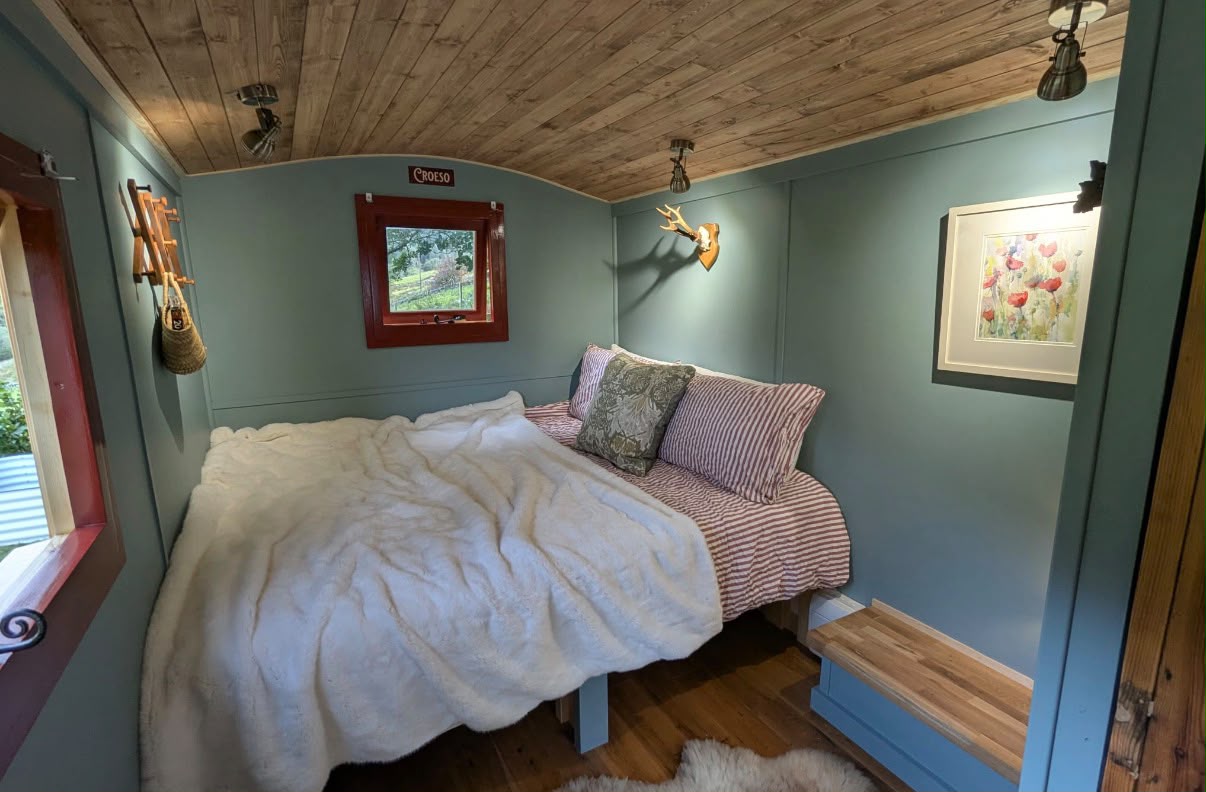 Bedroom inside a shepherd hut, with sage walls, a pine barrel ceiling and a double bed.