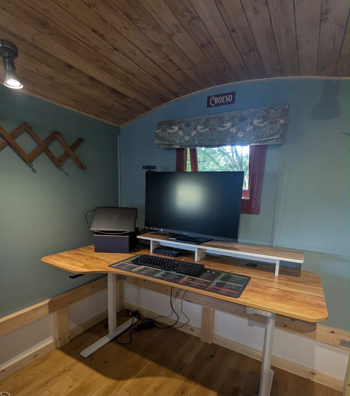 A home office inside a shepherd hut, with a desk, monitor and curved timber ceiling.