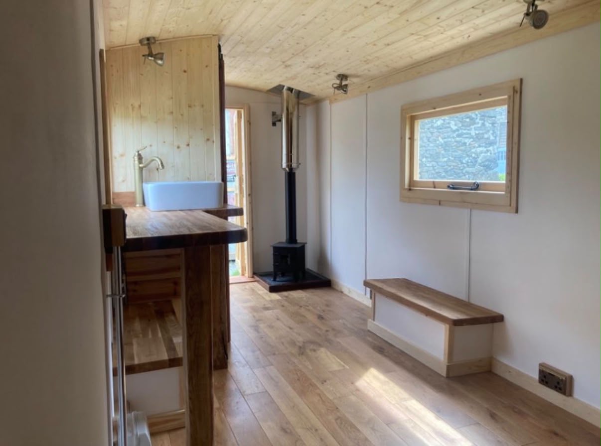 Inside a shepherd hut: pine ceiling, oak floor, wood burner, basin and bench seat.