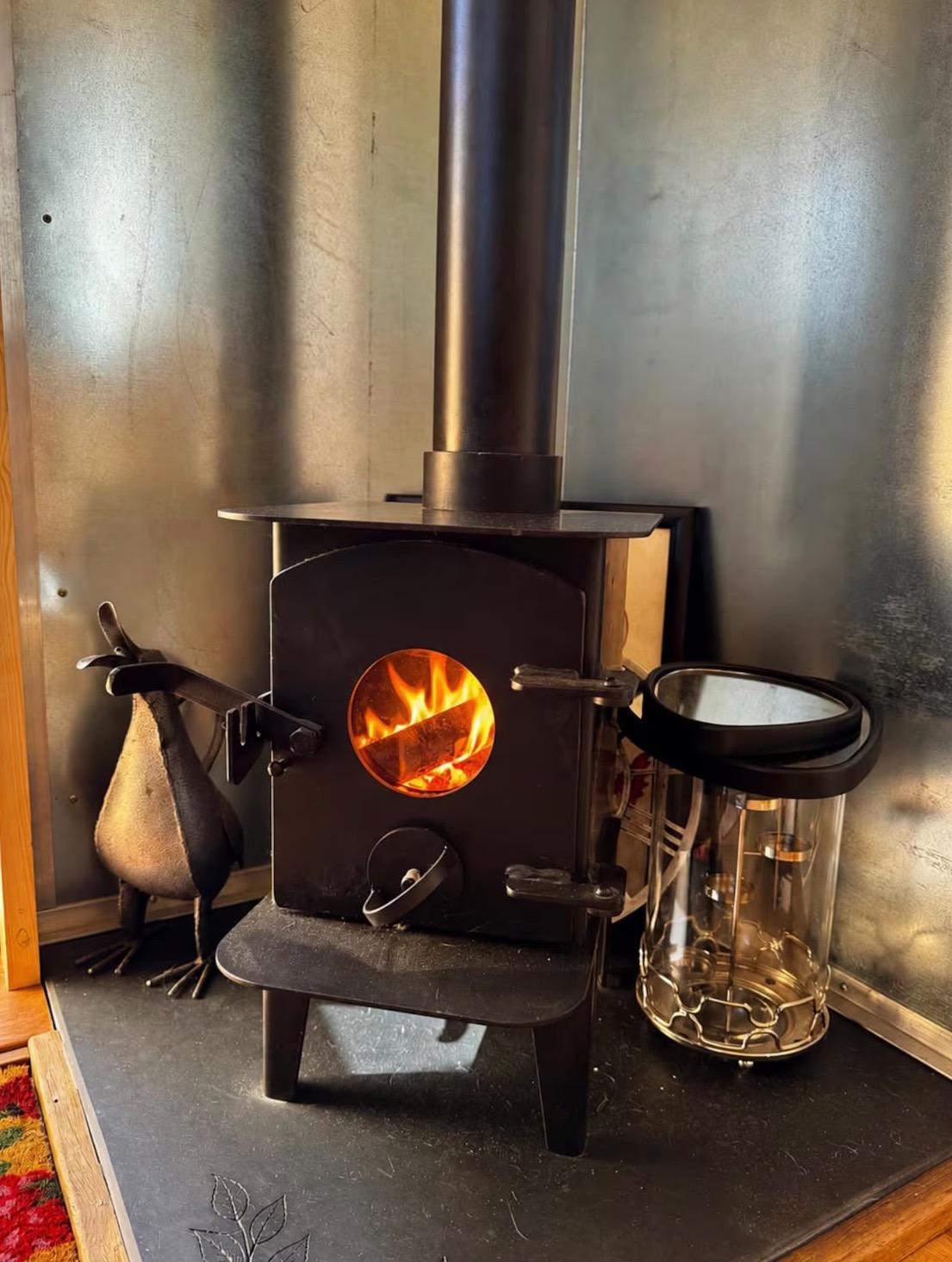 A lit wood burner in a shepherd hut, on a slate hearth with a galvanised backing.